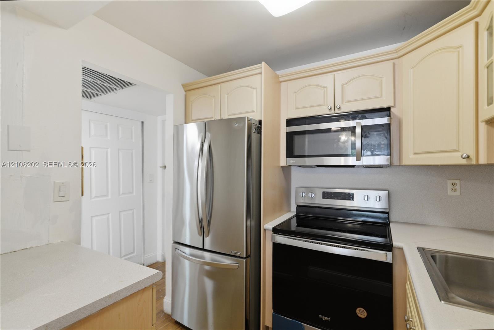 Kitchen featuring stainless steel French-door refrigerator, built-in microwave, electric range, solid-surface countertops, and light-tone cabinetry Kitchen featuring stainless steel French-door refrigerator, built-in microwave, electric range, solid-surface countertops, and light-tone cabinetry