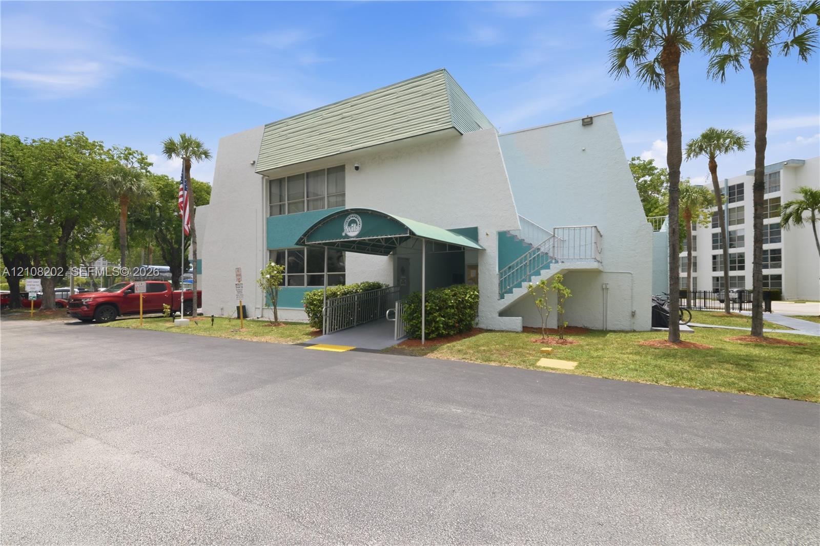 Two-story exterior featuring a textured stucco facade, a green arched awning, external metal staircase, and an asphalt parking area
