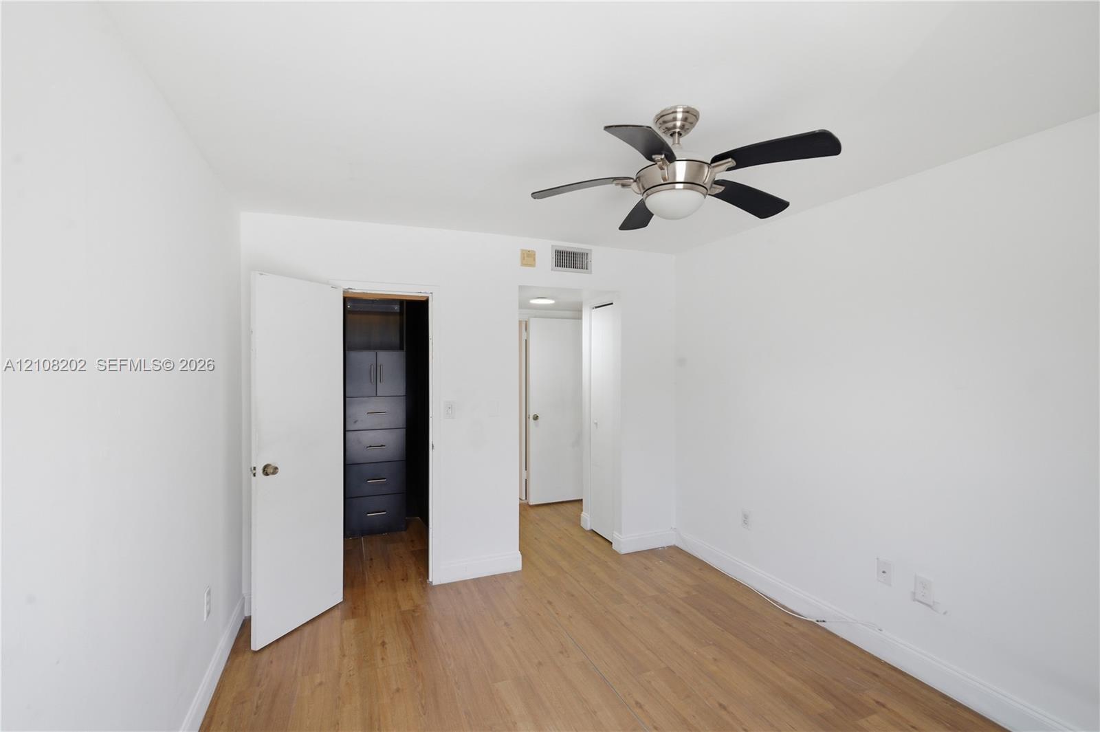 Room featuring wood-finish flooring, a multi-blade ceiling fan with integrated lighting, and built-in closet cabinetry