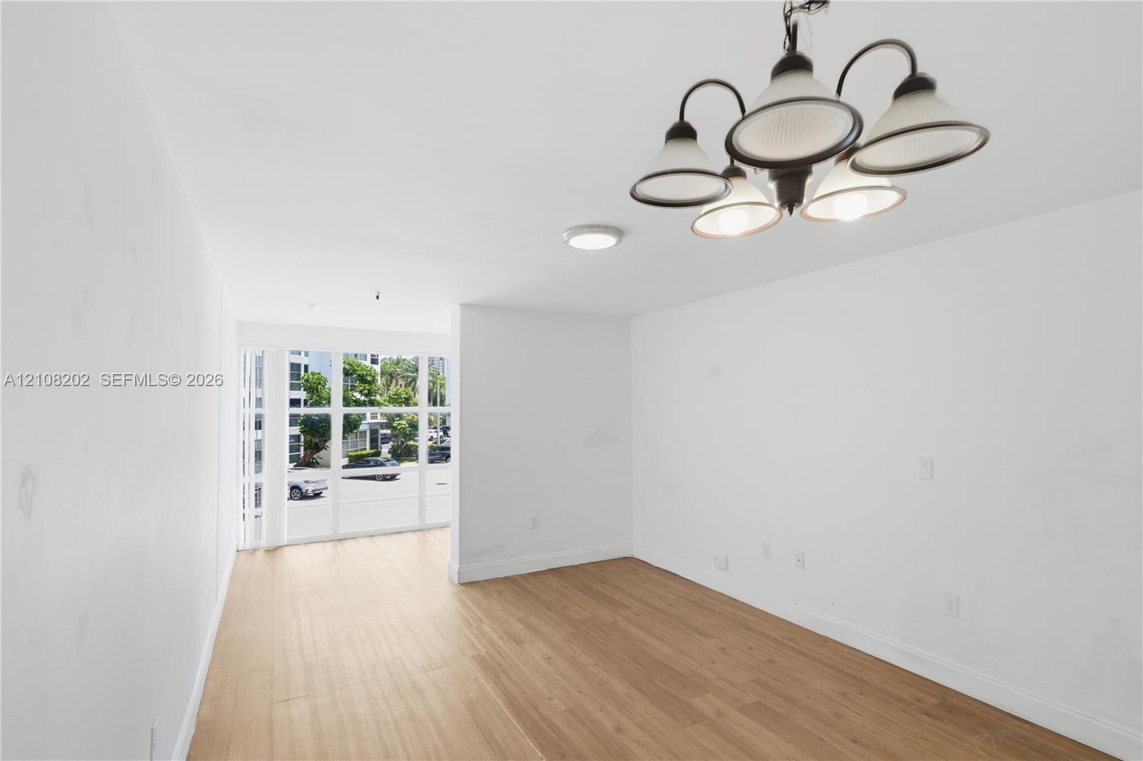 Interior space featuring wood-finish flooring, a five-arm chandelier, ceiling-mounted lighting, and large paneled windows Interior space featuring wood-finish flooring, a five-arm chandelier, ceiling-mounted lighting, and large paneled windows