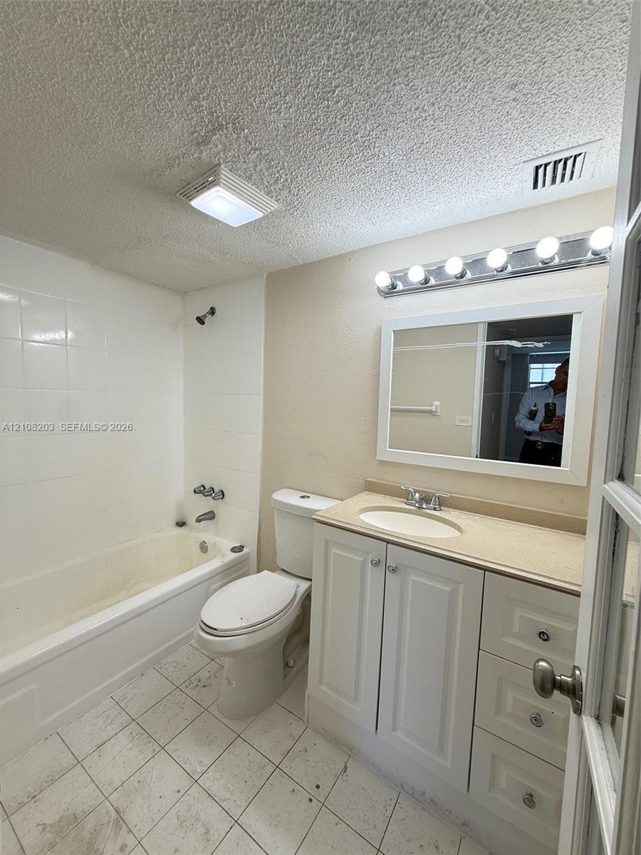 Bathroom featuring a white vanity cabinet with an integrated countertop and sink, a framed mirror, a multi-bulb vanity light fixture, and a tiled shower surround