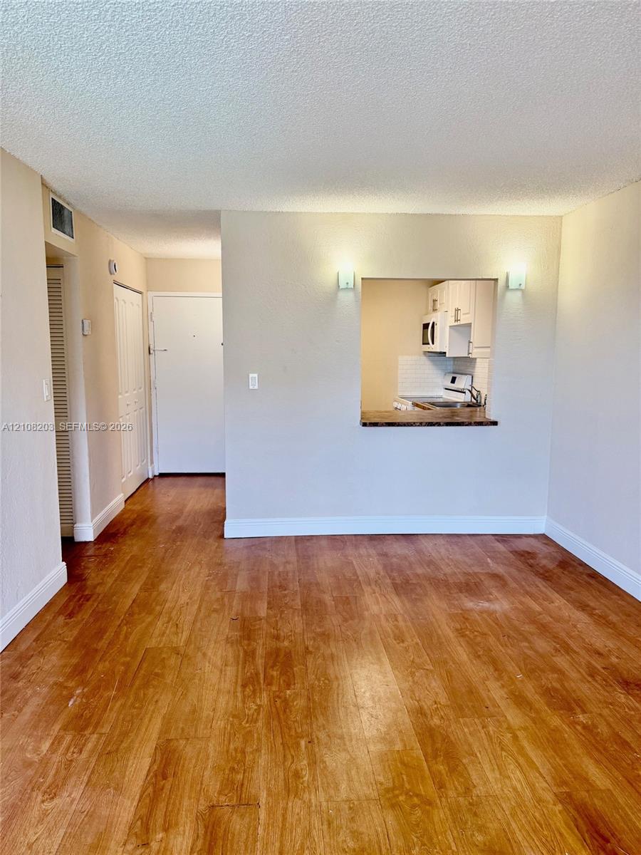 Wood-finish flooring throughout, wall-mounted light fixtures, and a pass-through opening with a solid-surface ledge