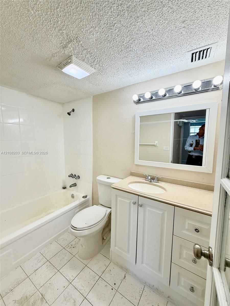 Bathroom featuring a white vanity cabinet with an integrated sink, neutral countertop, rectangular mirror with a chrome five-light fixture, and a tiled shower-tub combination