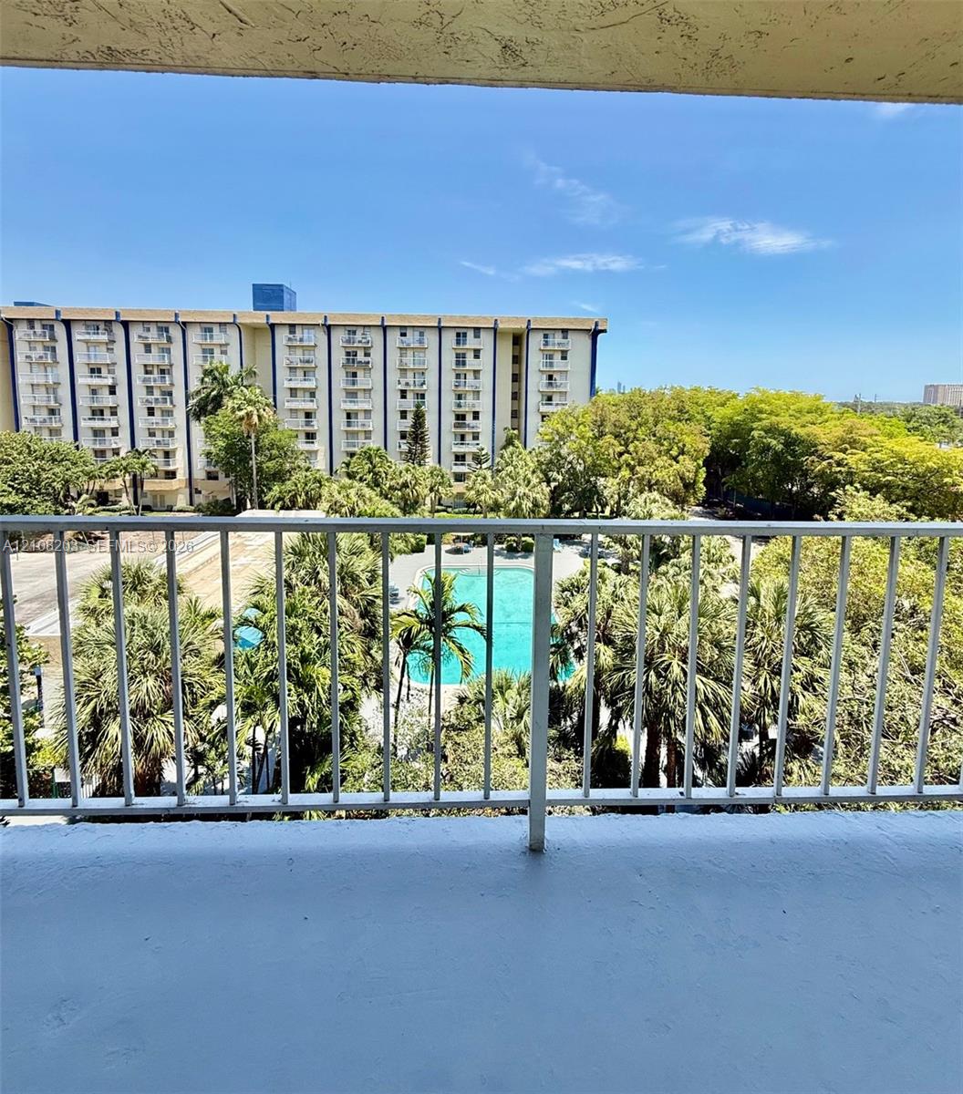 Open-air balcony featuring white metal railings, overlooking an outdoor swimming pool, paved hardscaping, and mature palm trees