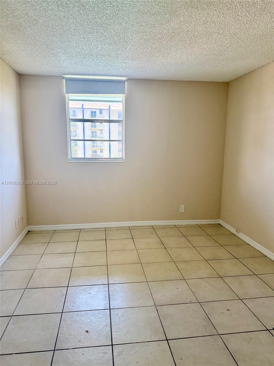 Interior space featuring neutral wall tones, large-format ceramic floor tiles, and a window with a roller shade