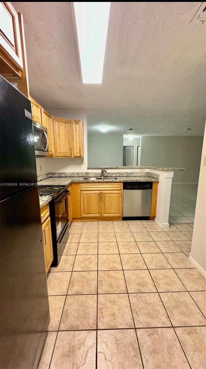 Kitchen featuring light wood cabinetry, stone-finish countertops, stainless steel dishwasher, integrated range and microwave, and ceramic tile flooring
