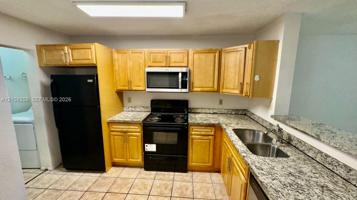 Kitchen featuring light-finish cabinetry, stone-patterned countertops, a stainless steel double-basin sink, a built-in microwave, and ceramic tile flooring
