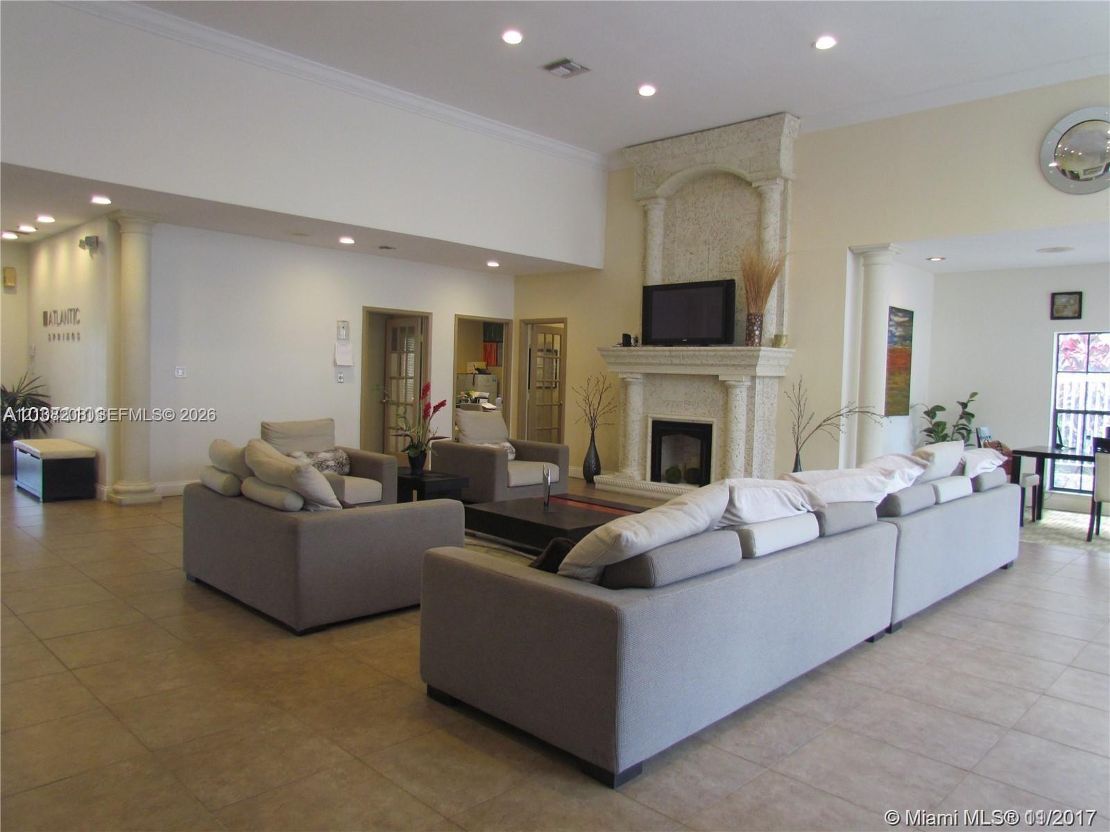 Open-concept living space featuring high ceilings, recessed lighting, tile flooring, and a stone-clad fireplace with architectural columns