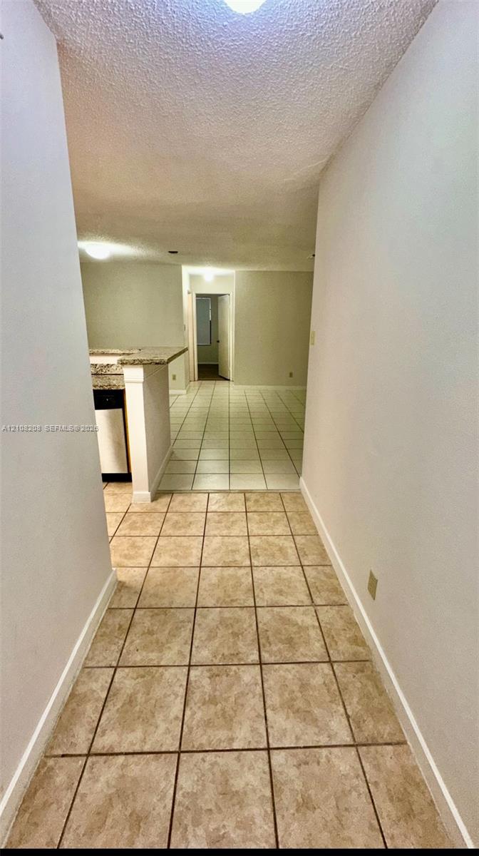Interior hallway featuring tile flooring, neutral wall tones, and stone-surfaced counter peninsula