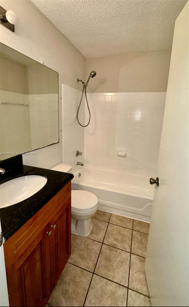 Bathroom featuring wood-finish cabinetry, a dark countertop with an integrated white sink, tile flooring, and a shower-tub combination with white wall tile