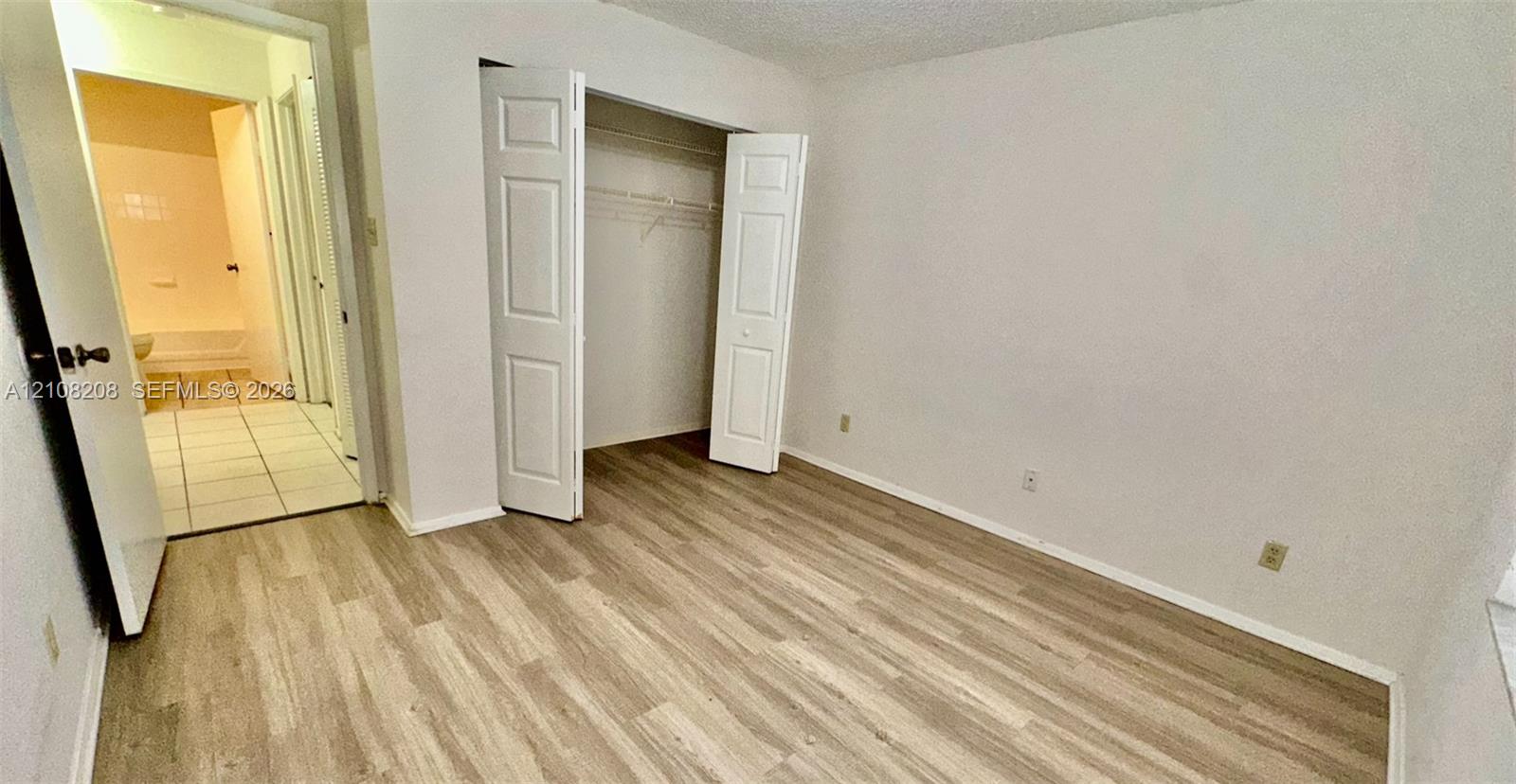 Room featuring wood-finish flooring, a bi-fold door closet with built-in shelving, and entry to a tiled space