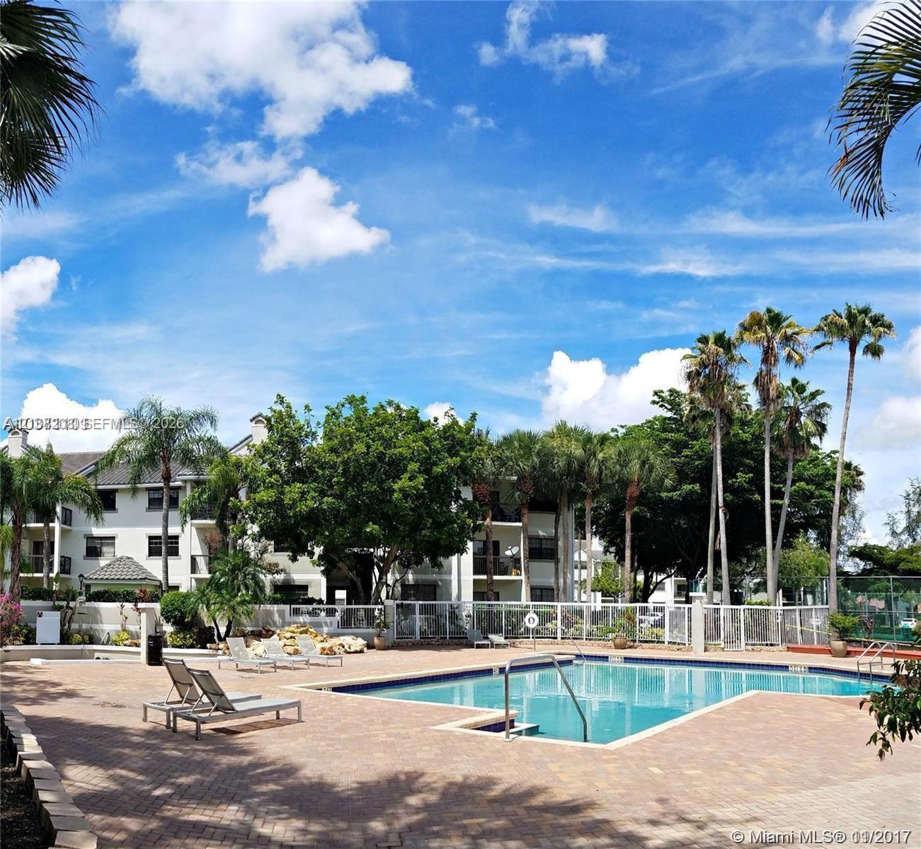 In-ground swimming pool with brick paver decking, surrounding perimeter fencing, and mature palm trees