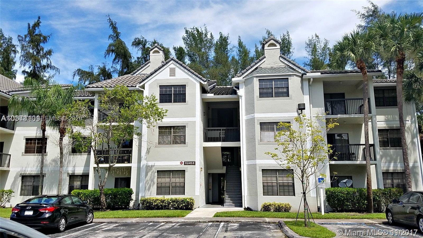 Multi-story stucco exterior featuring a pitched tile roof, private balconies with metal railings, and prominent gabled architectural accents