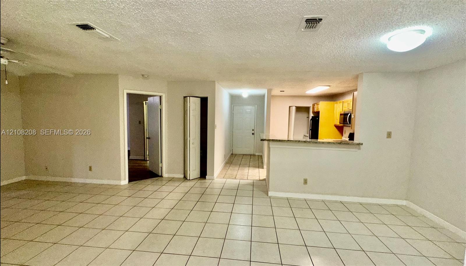 Neutral-toned tile flooring, pass-through kitchen counter, ceiling-mounted lighting, and folding closet door