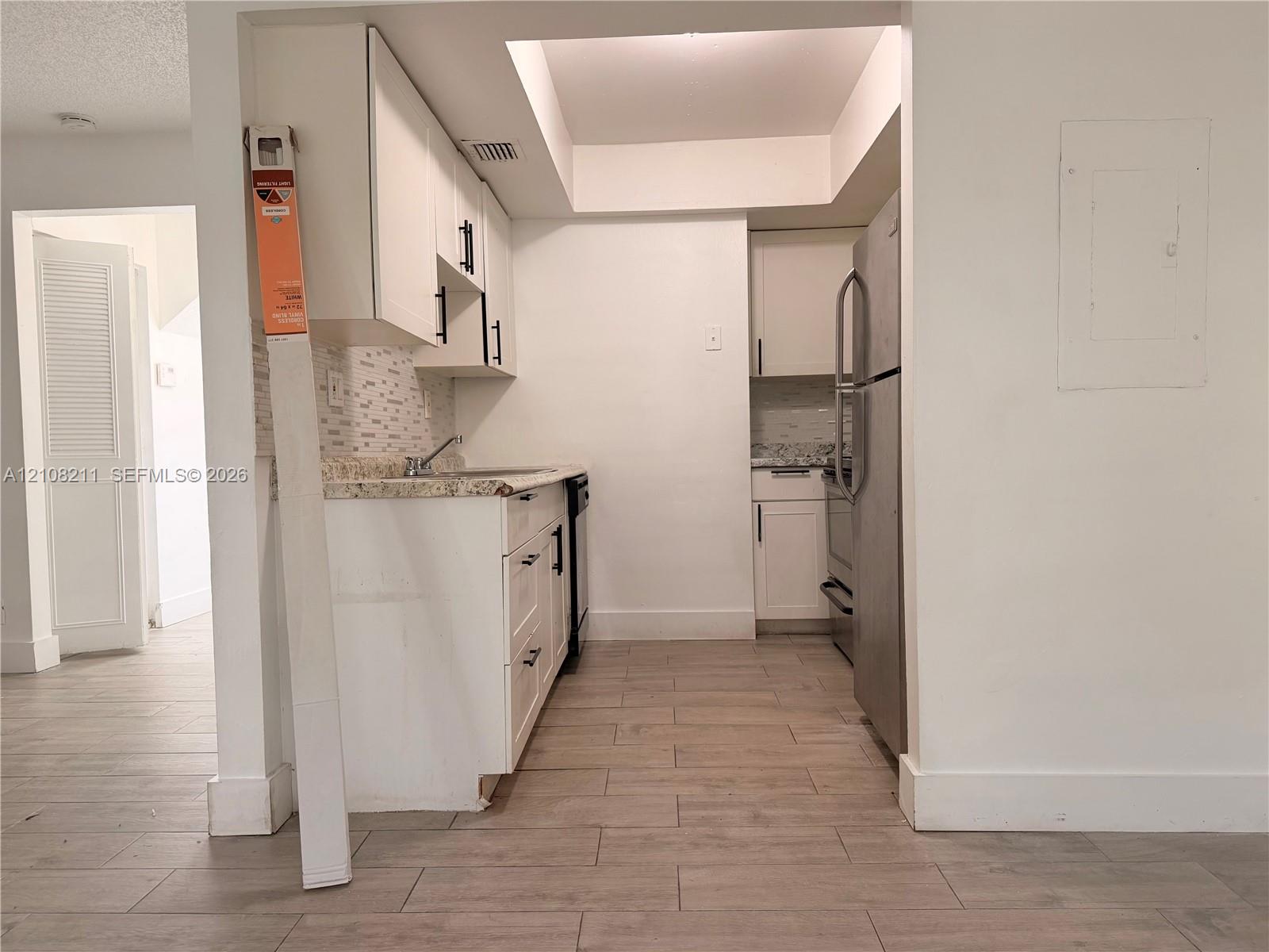 Kitchen featuring white cabinetry with matte black hardware, stone-patterned countertops, a tiled backsplash, stainless steel refrigerator, and wood-finish flooring
