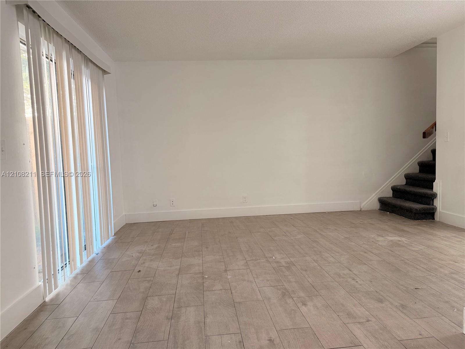 Neutral interior featuring wood-finish tile flooring, vertical window blinds, and a staircase with carpeted treads