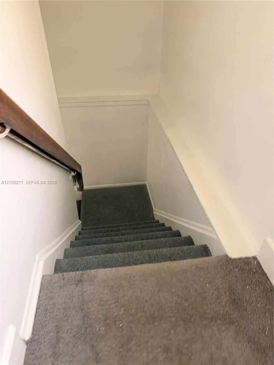 Carpeted staircase featuring a wooden handrail and white wall finishes