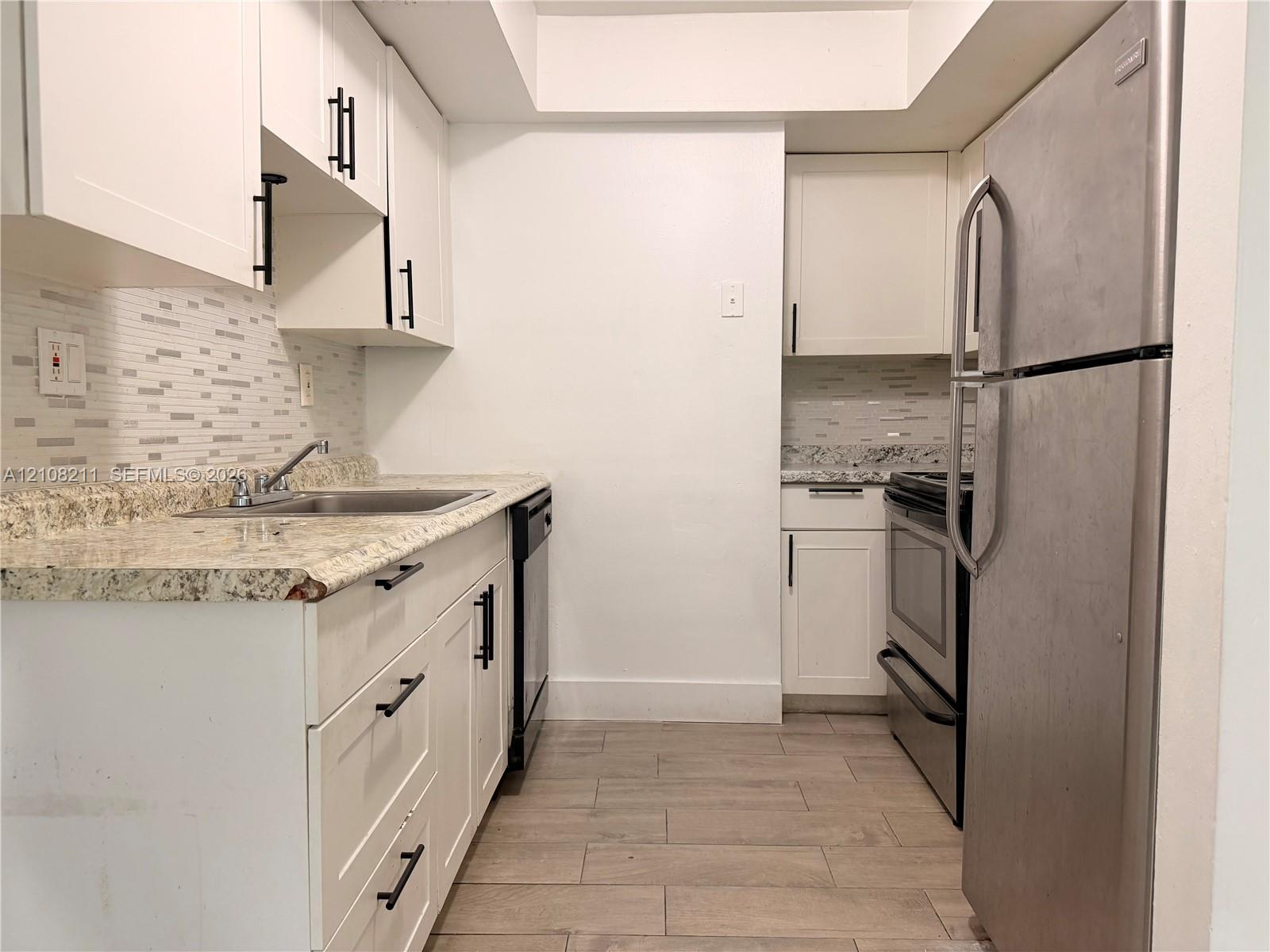 Kitchen featuring white shaker-style cabinetry, stone-surface countertops, mosaic tile backsplash, stainless steel appliances, and wood-finish flooring