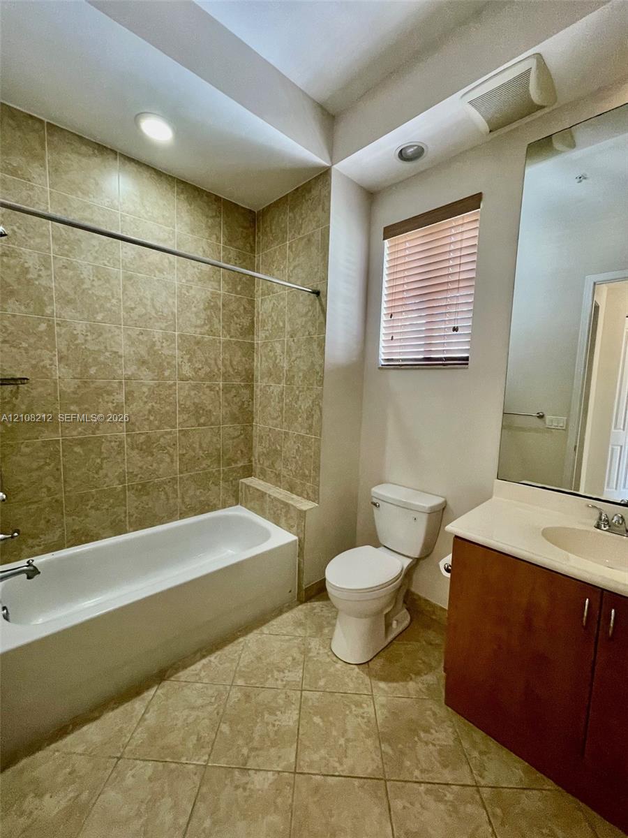 Bathroom featuring a tiled tub-shower surround, vanity with an integrated countertop sink, large wall-mounted mirror, and tile flooring
