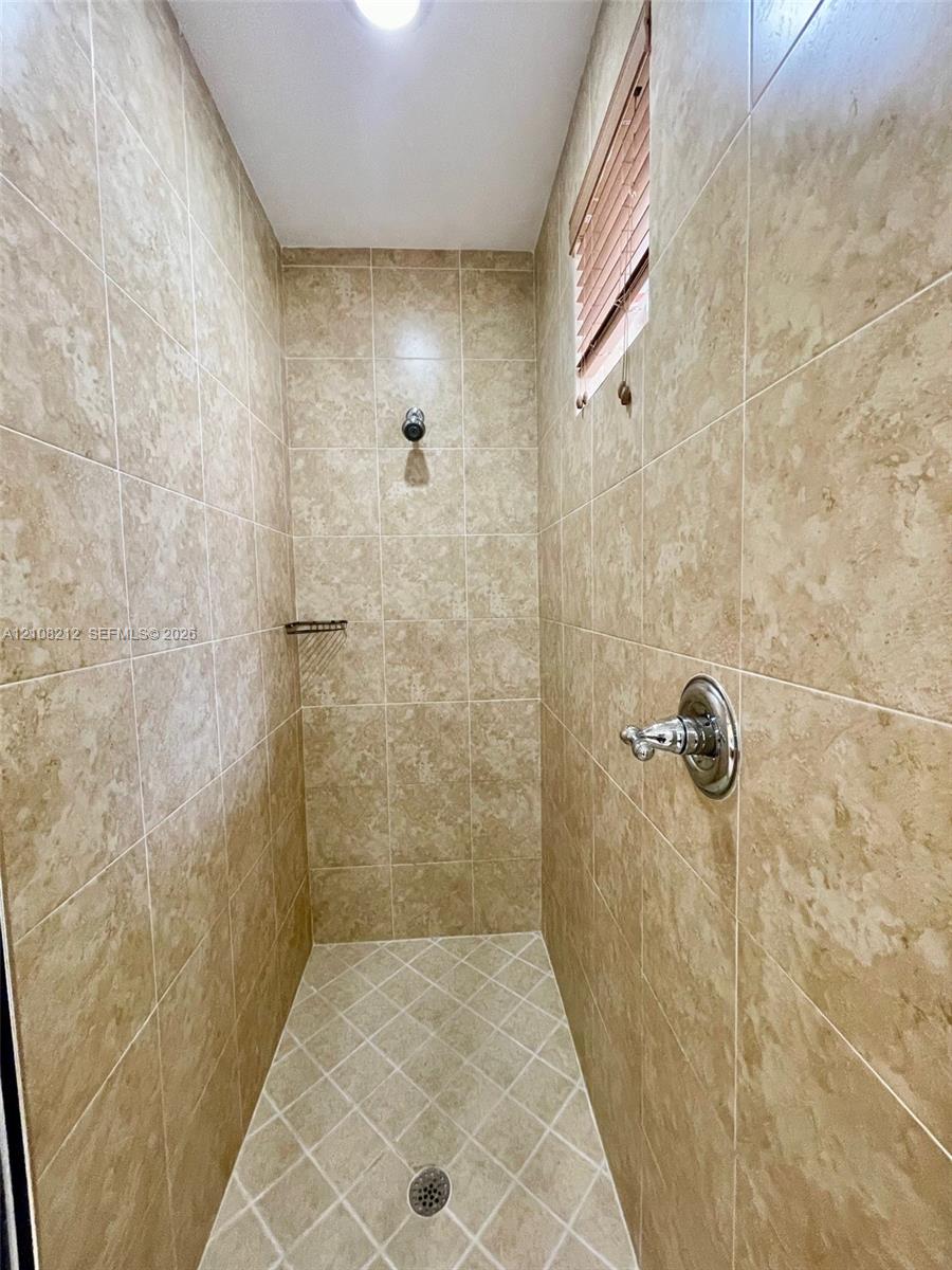 Shower stall featuring full-height neutral-toned tile walls, a diamond-patterned tile floor, recessed lighting, and integrated metal shower fixtures