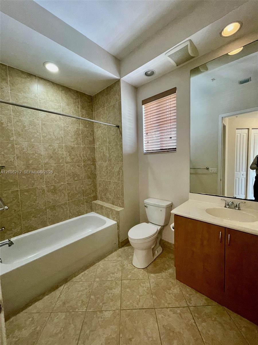 Bathroom featuring a tub-shower combination with tiled surround, large vanity with countertop sink, recessed ceiling lighting, and tile flooring