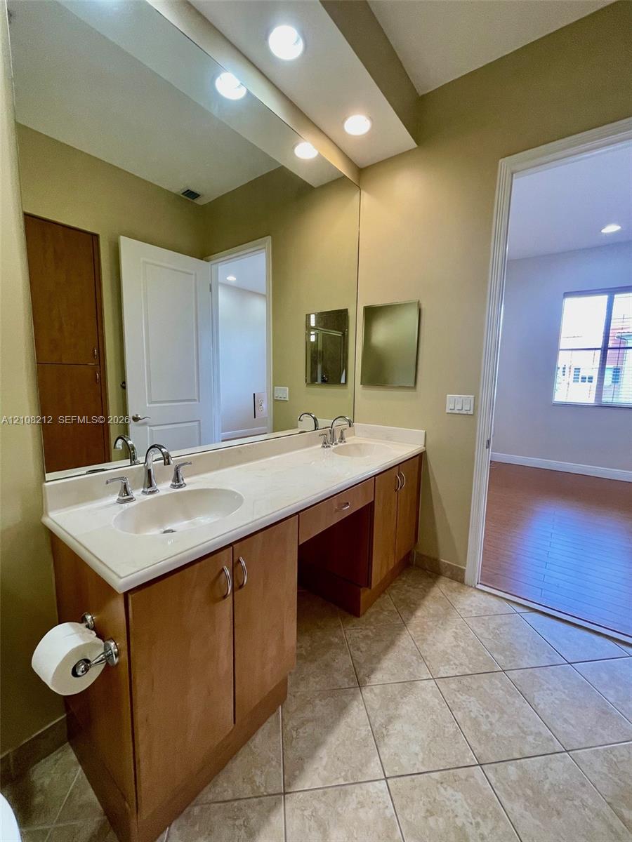 Dual-sink vanity with light-tone cabinetry, solid surface countertop, inset rectangular mirrors, recessed ceiling lighting, and ceramic tile flooring