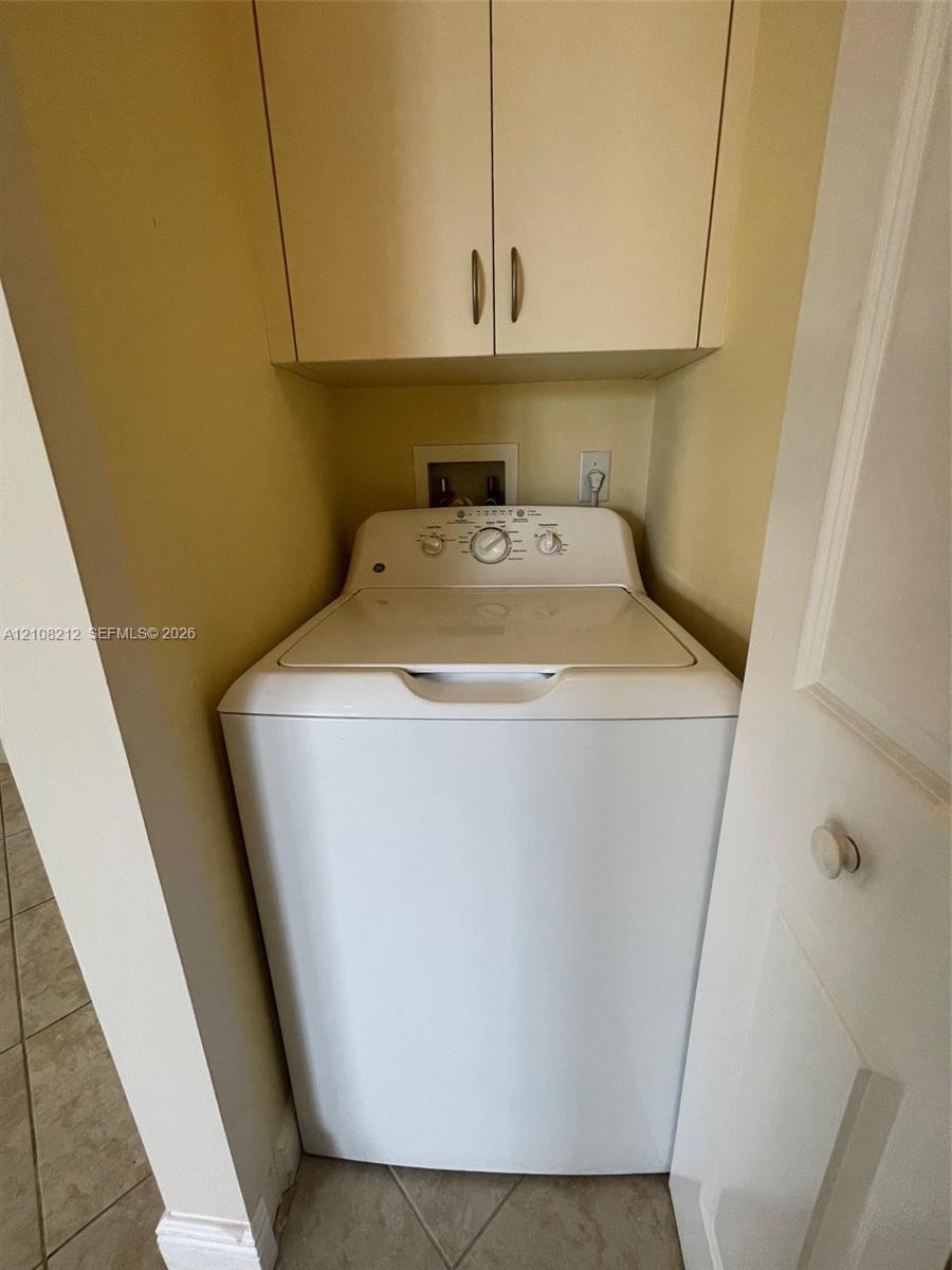 Built-in laundry alcove featuring overhead storage cabinetry and tiled flooring