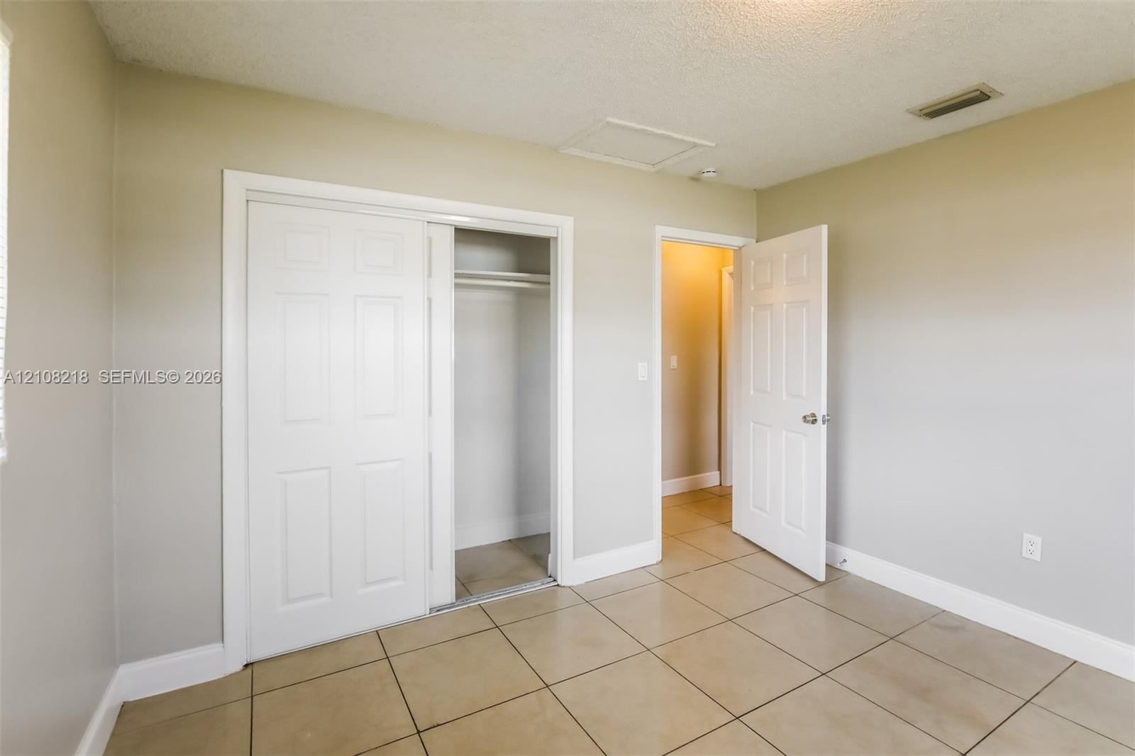 Neutral-toned interior featuring ceramic tile flooring, sliding bypass closet doors, and traditional six-panel interior doors Neutral-toned interior featuring ceramic tile flooring, sliding bypass closet doors, and traditional six-panel interior doors
