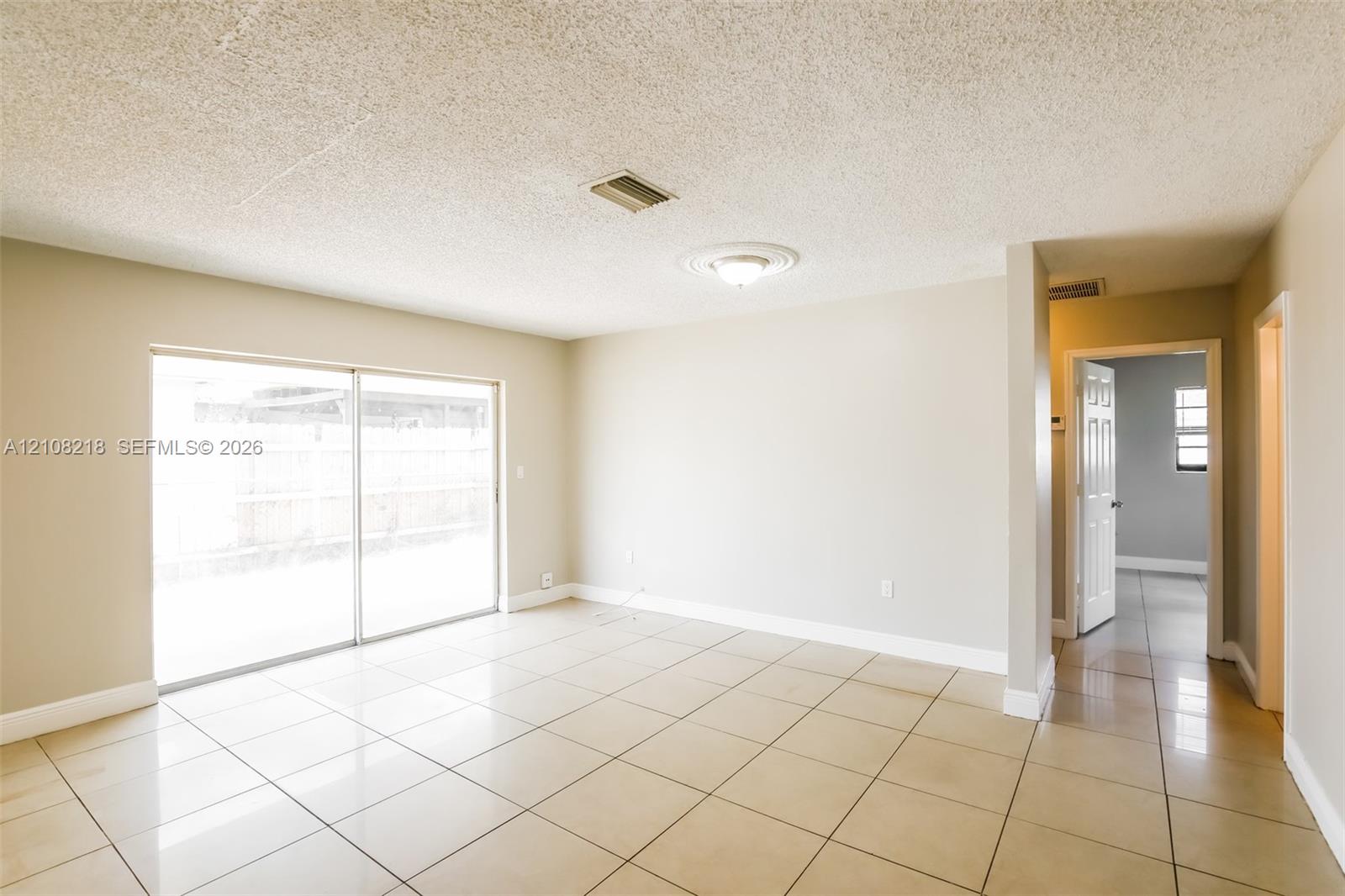 Neutral-toned interior space featuring light-colored ceramic tile flooring, sliding glass doors, a ceiling-mounted light fixture with medallion detail, and textured ceiling finish Neutral-toned interior space featuring light-colored ceramic tile flooring, sliding glass doors, a ceiling-mounted light fixture with medallion detail, and textured ceiling finish