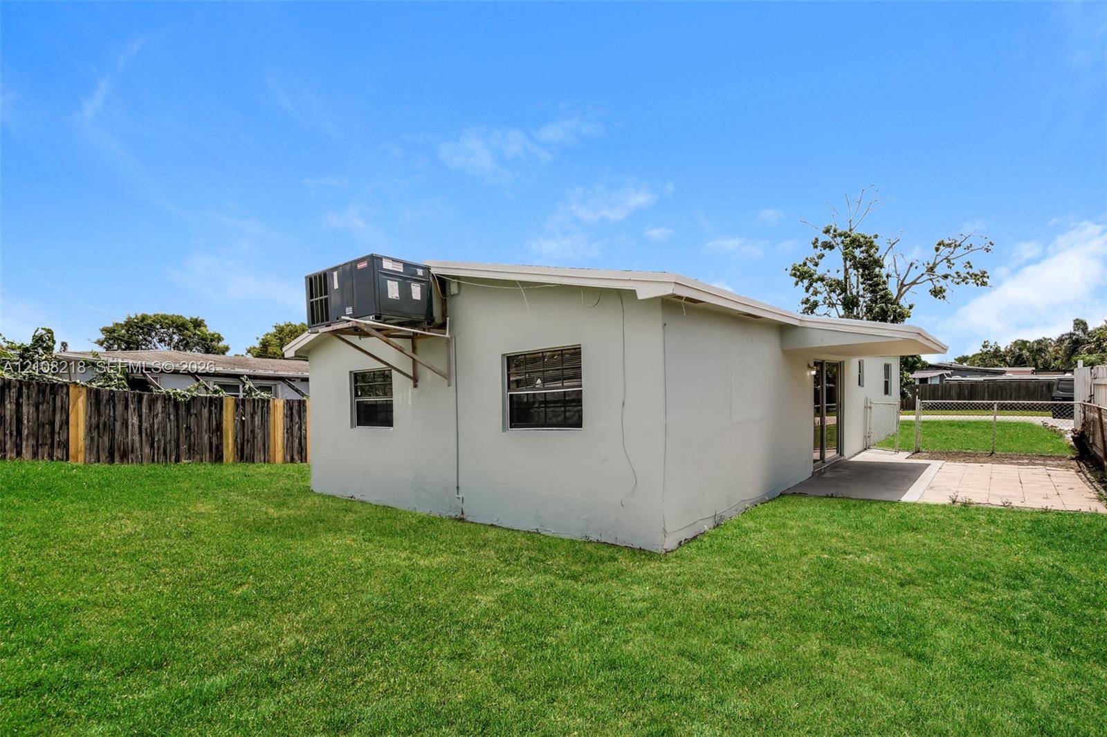 Exterior featuring a stucco facade, concrete patio, expansive grass lawn, wood perimeter fencing, and an exterior mounted HVAC unit