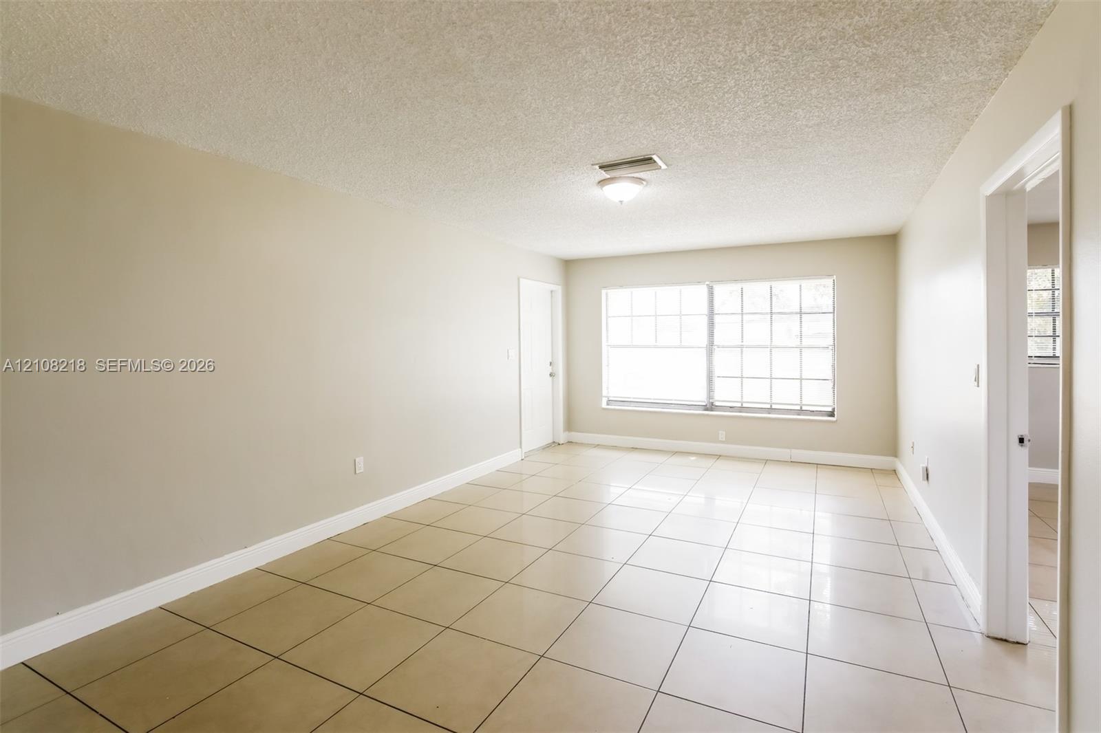 Neutral-toned interior space featuring ceramic tile flooring, a large multi-pane window, and a central flush-mount ceiling light fixture Neutral-toned interior space featuring ceramic tile flooring, a large multi-pane window, and a central flush-mount ceiling light fixture