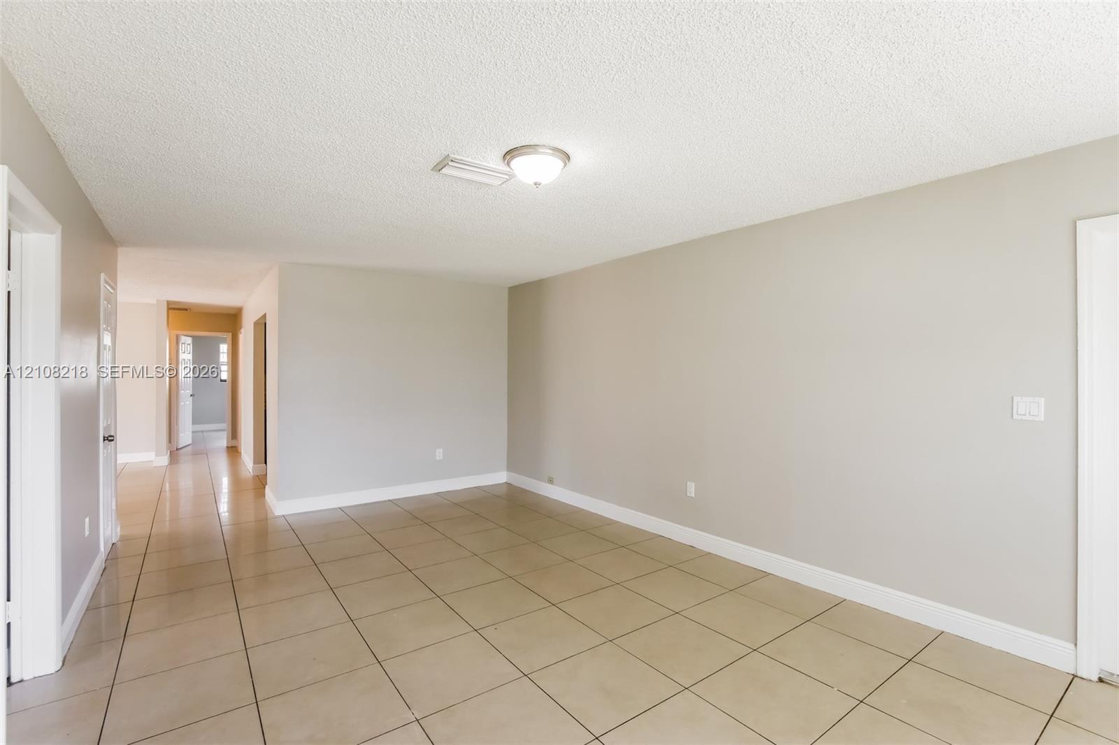 Neutral-toned interior space featuring light-colored square floor tiling, crisp white door frames, and a flush-mount ceiling light fixture Neutral-toned interior space featuring light-colored square floor tiling, crisp white door frames, and a flush-mount ceiling light fixture