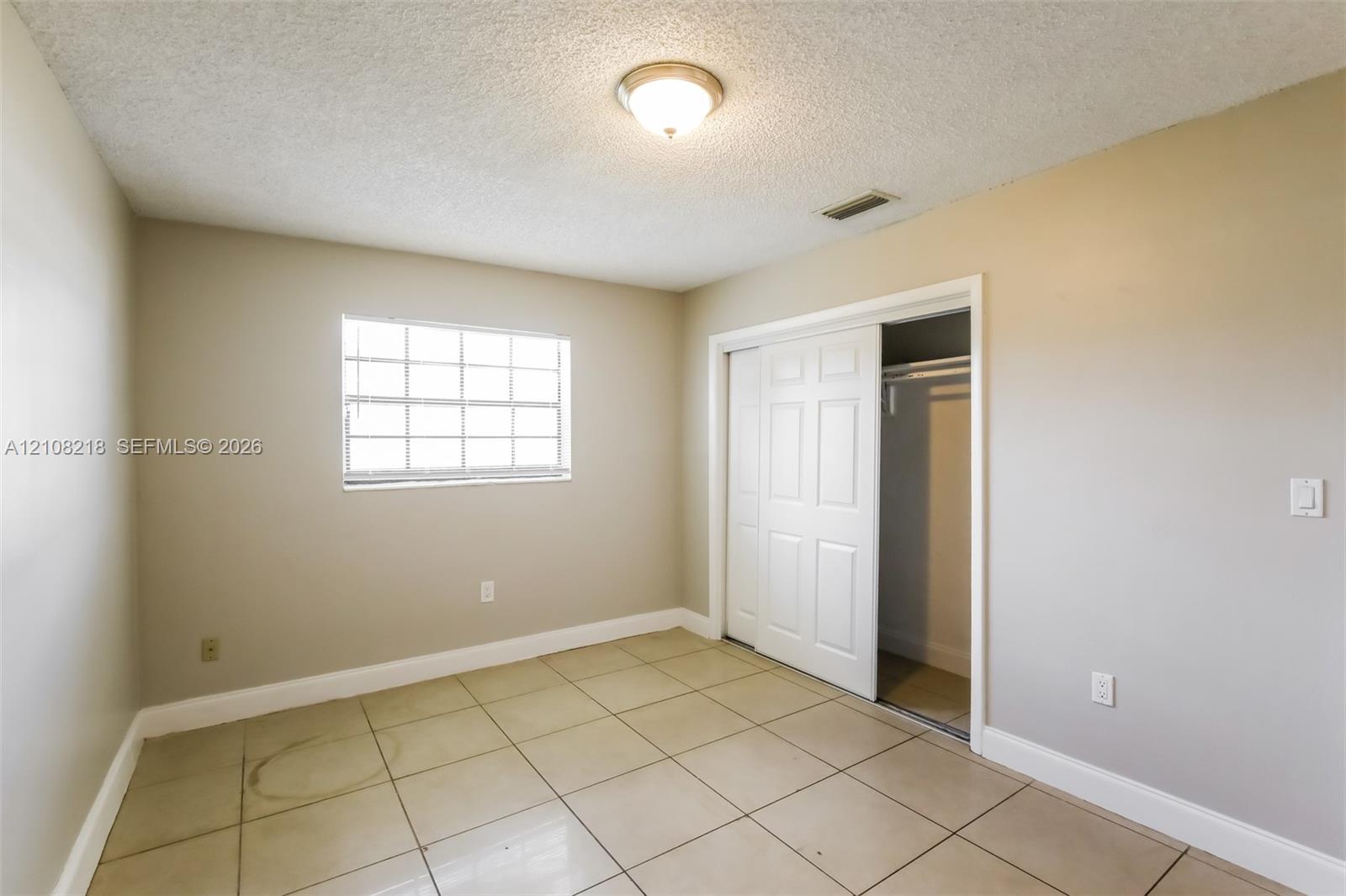 Neutral-toned room featuring large-format square tile flooring, a multi-pane window, and a built-in closet with white paneled sliding doors Neutral-toned room featuring large-format square tile flooring, a multi-pane window, and a built-in closet with white paneled sliding doors