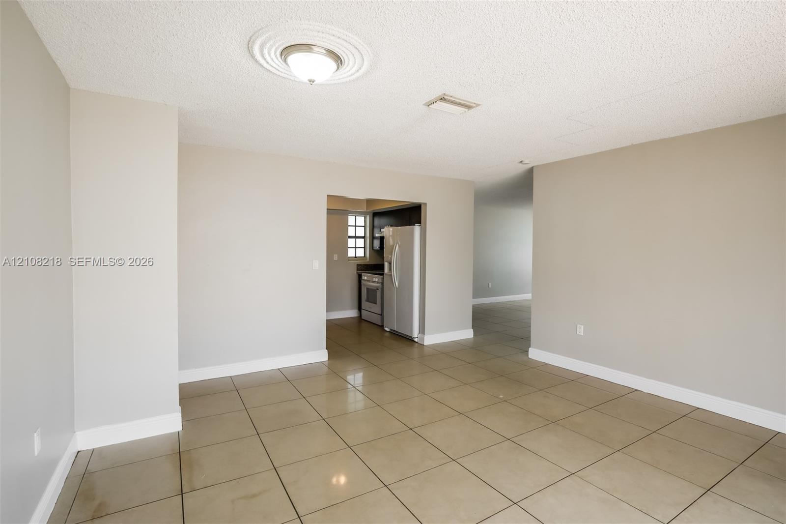 Neutral-toned interior featuring large-format tile flooring, a ceiling medallion with a flush-mount light fixture, and visible kitchen cabinetry with stainless steel appliances Neutral-toned interior featuring large-format tile flooring, a ceiling medallion with a flush-mount light fixture, and visible kitchen cabinetry with stainless steel appliances