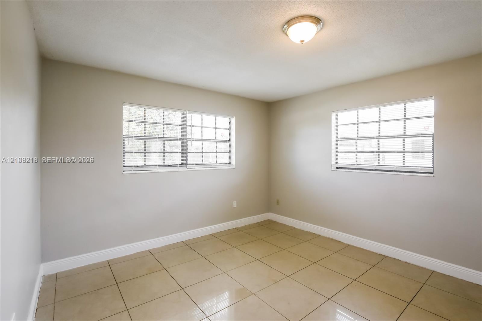 Room featuring neutral wall paint, polished tile flooring, dual windows with grid detailing, and a flush-mount ceiling light fixture