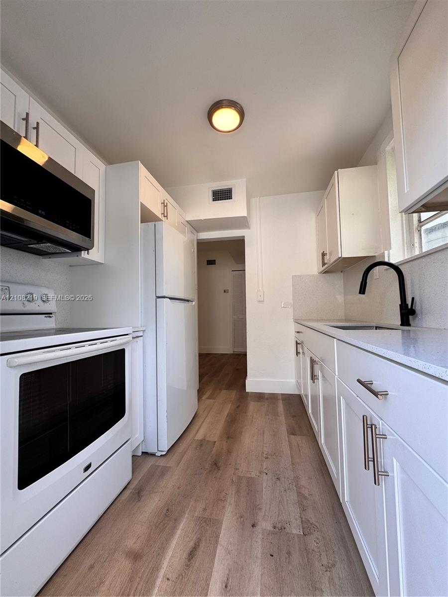 Kitchen featuring white shaker-style cabinetry, solid-surface countertops, wood-finish flooring, a stainless steel microwave, and a matte black faucet
