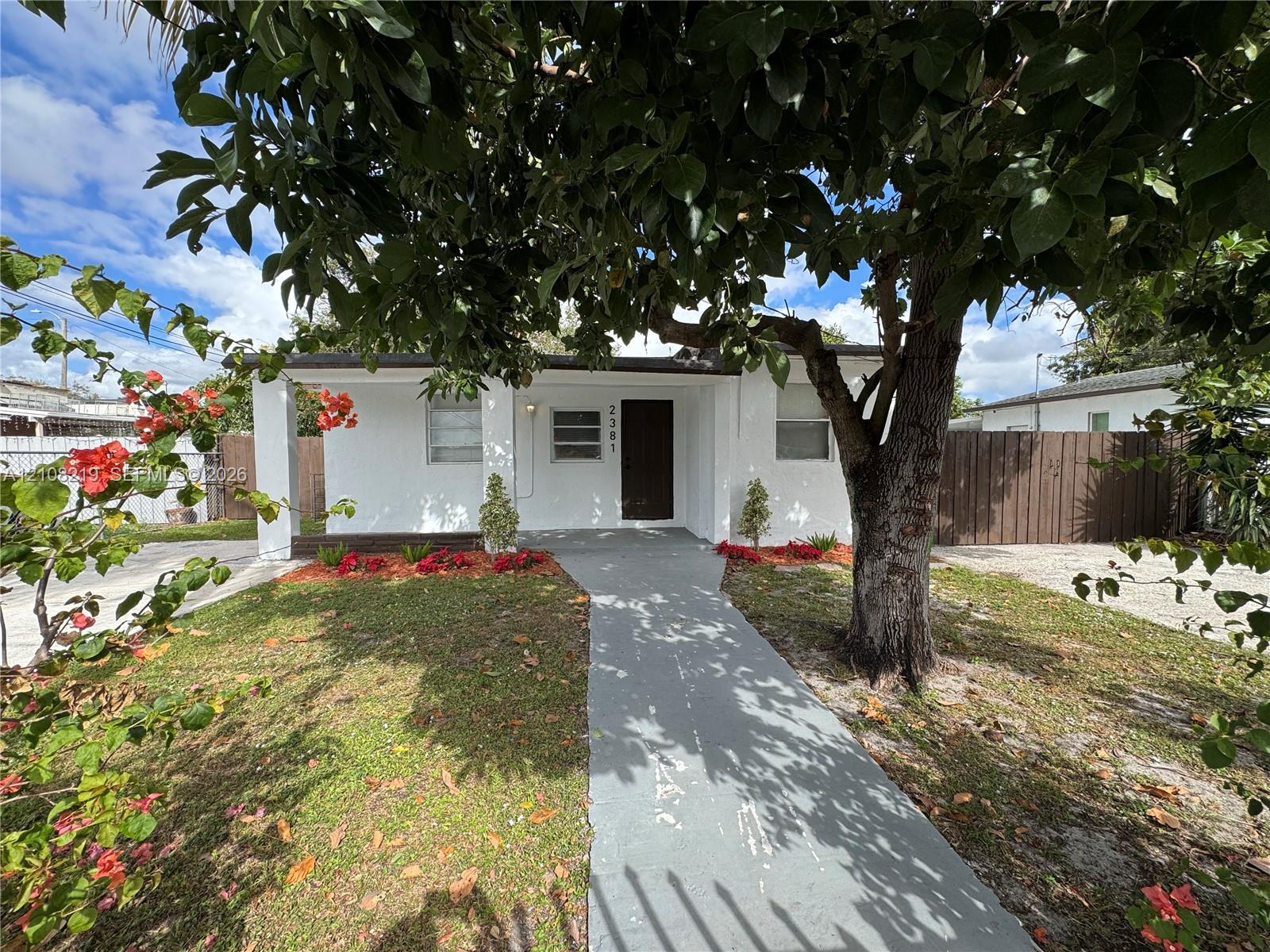 Single-story exterior featuring a painted stucco facade, covered porch, horizontal jalousie windows, and mature landscaping