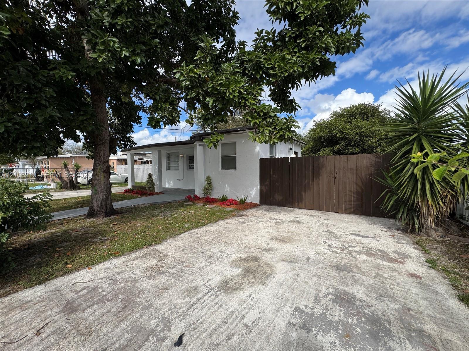 Stucco exterior featuring a concrete driveway, covered porch entrance, and wood-panel privacy fencing