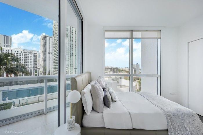 Floor-to-ceiling windows, high-rise urban scenery, glass-paneled balcony, and neutral tile flooring