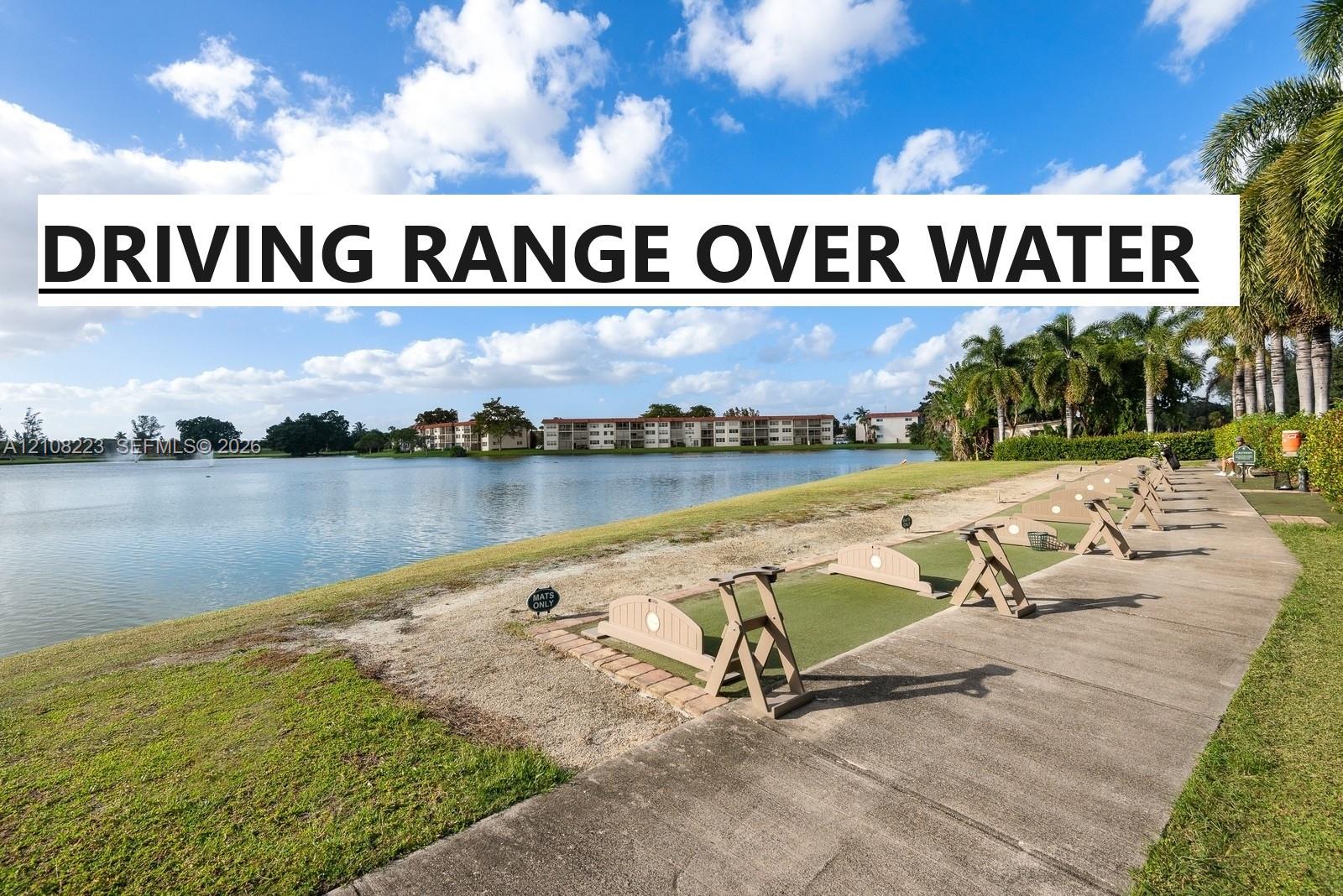 Golf driving range featuring synthetic turf hitting stations, brick edging, concrete walkway, and water feature