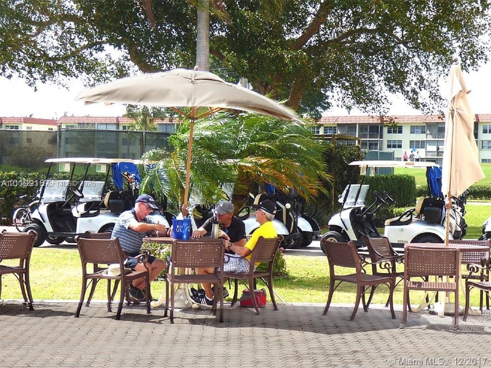 Paver patio area featuring mature tree canopy, landscaping, and golf course access