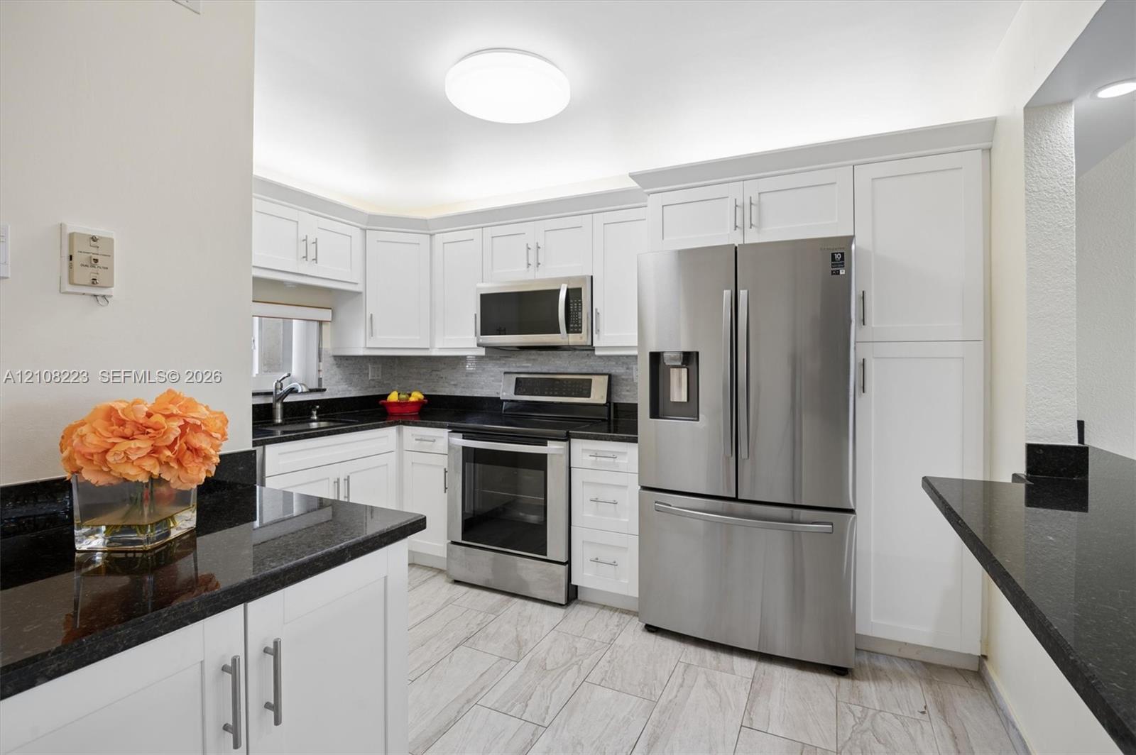 Kitchen featuring white shaker-style cabinetry, black stone countertops, stainless steel appliances, and tile flooring