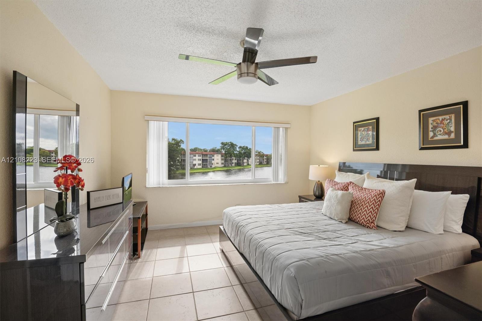 Large horizontal window featuring water scenery, neutral tile flooring, and a modern ceiling fan