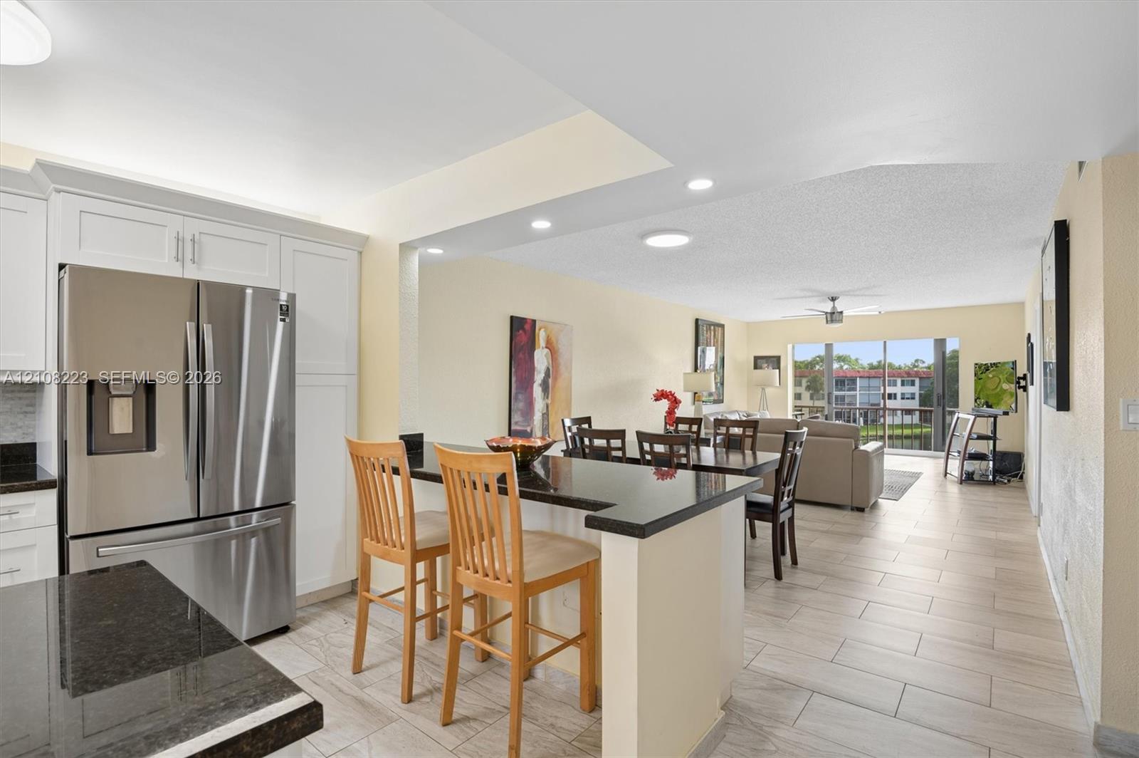 Kitchen featuring white shaker-style cabinetry, dark stone countertops, stainless steel refrigerator, recessed lighting, and ceramic tile flooring