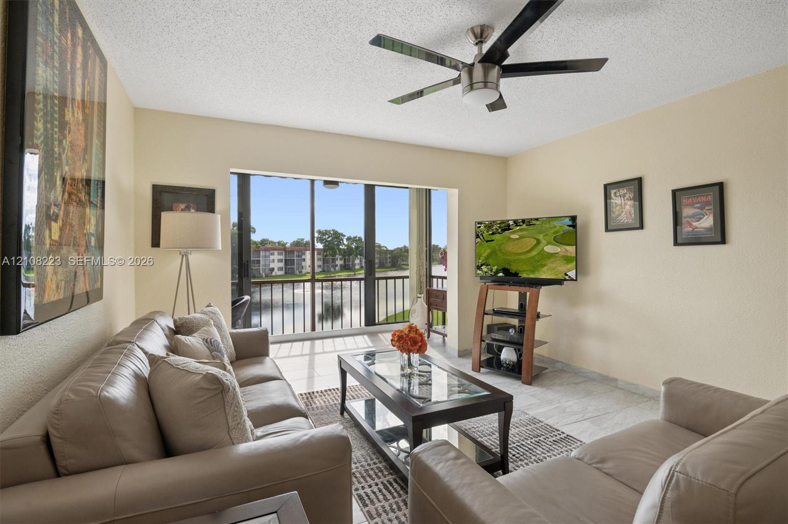 Living area featuring large format tile flooring, a multi-blade ceiling fan, and floor-to-ceiling glass sliding doors opening to a railed balcony