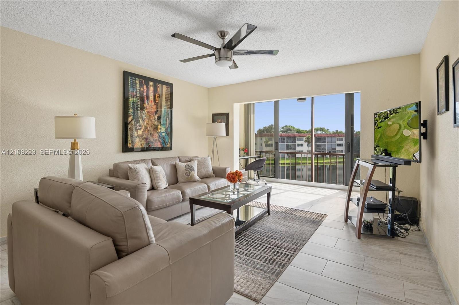 Living area featuring large-format tile flooring, a central multi-blade ceiling fan, and floor-to-ceiling sliding glass doors opening to a screened balcony