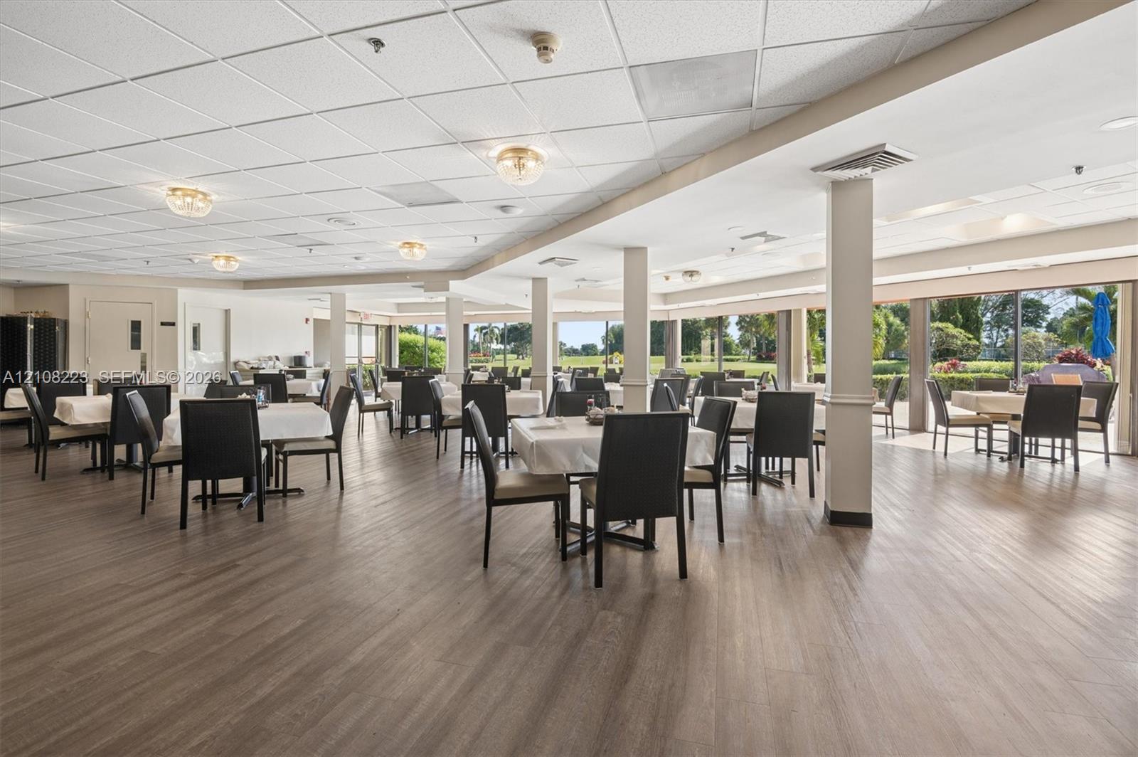Open-concept interior featuring wood-finish flooring, drop ceiling panels, structural support columns, and large-format glass sliding doors