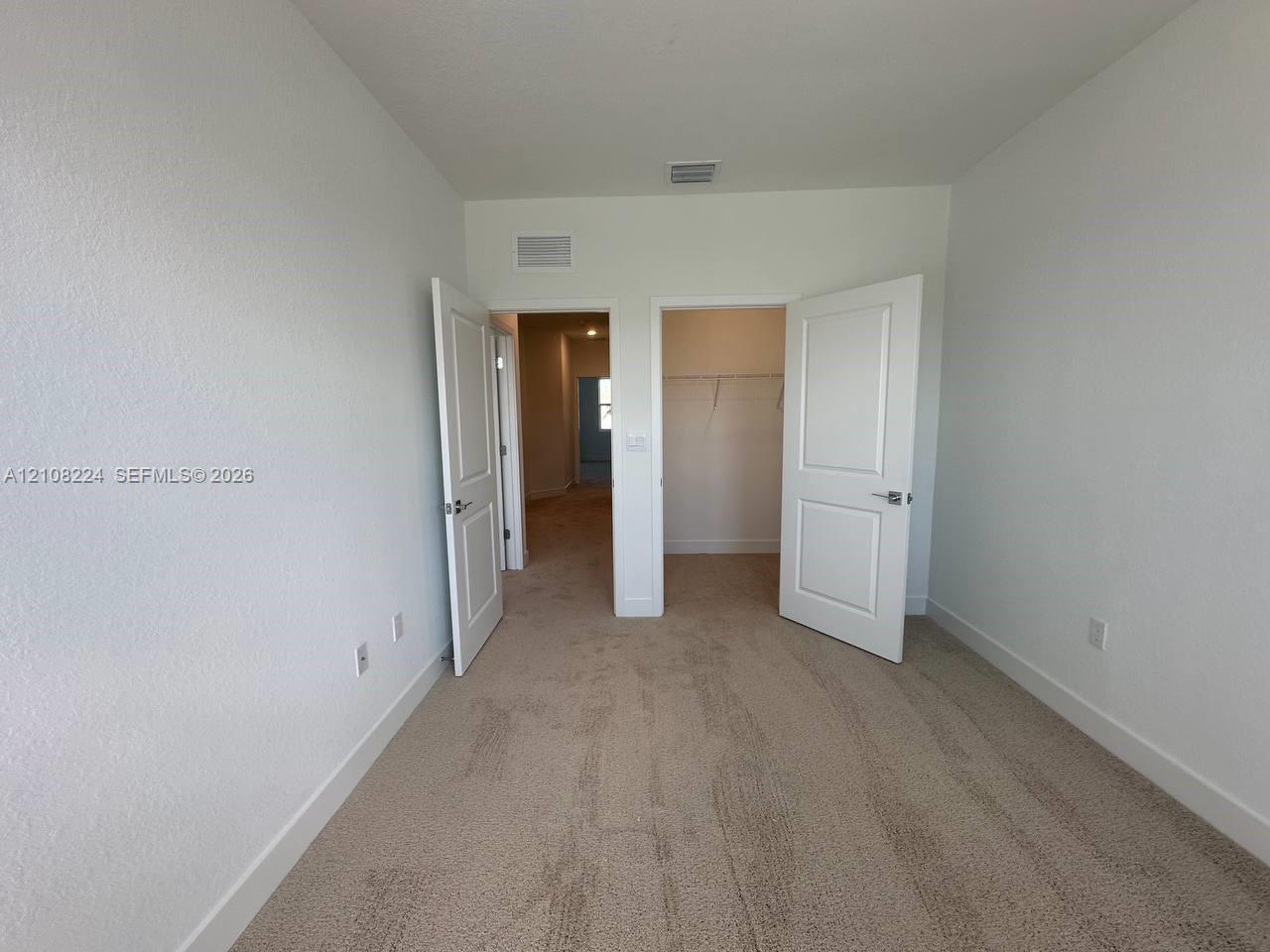 Room featuring neutral-toned carpeting, two interior doorways with paneled doors, and a reach-in closet with integrated wire shelving