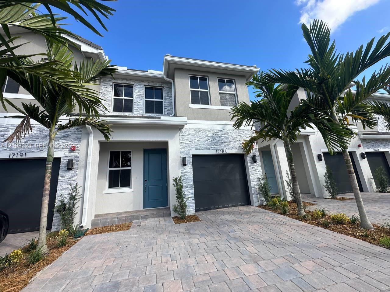 Two-story exterior featuring a stone veneer facade, paver driveway, solid-color entry door, and attached garage