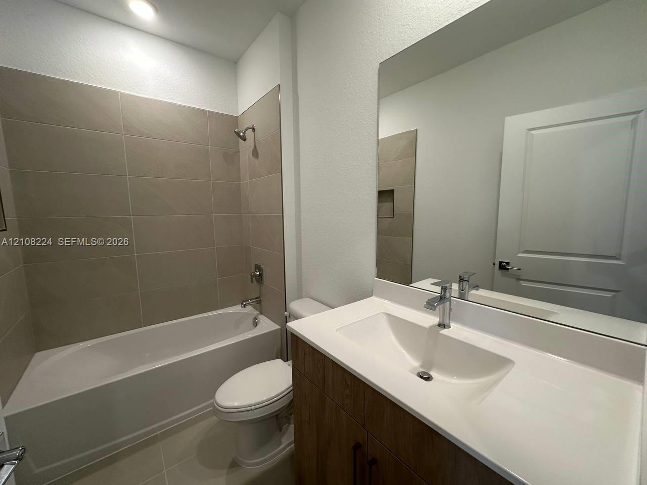 Bathroom featuring a vanity with a white integrated sink, wood-finish cabinetry, a large wall-mounted mirror, and a tiled shower-tub combination